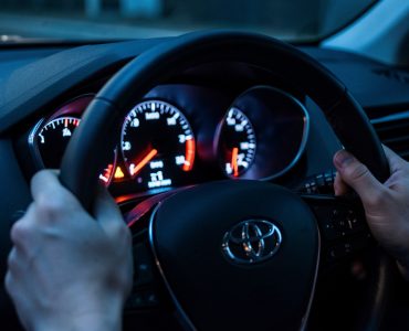 Vue nocturne réaliste du tableau de bord d’une voiture, avec le voyant moteur allumé et des détails des jauges éclairés dans une ambiance informative.